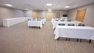 A conference room with multiple tables and chairs, carpeted floor, and a wooden door.