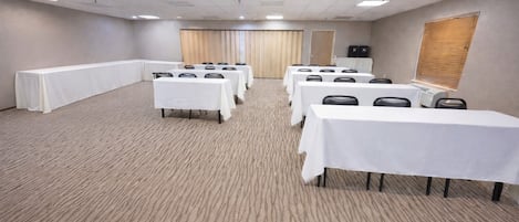 A conference room with multiple tables and chairs, carpeted floor, and a wooden door.