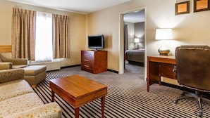 A hotel room with a sofa, a wooden table, a TV on a stand, a desk with a lamp, and a bed in the background. - Comfort Inn Owatonna near Medical Center (Owatonna)