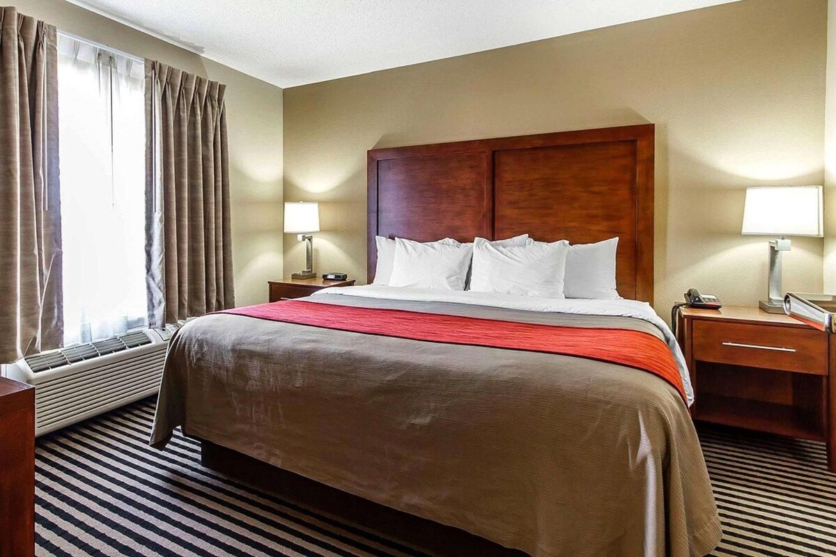 A hotel room with a large bed, two bedside tables, a window with curtains, and a wall-mounted heater.
