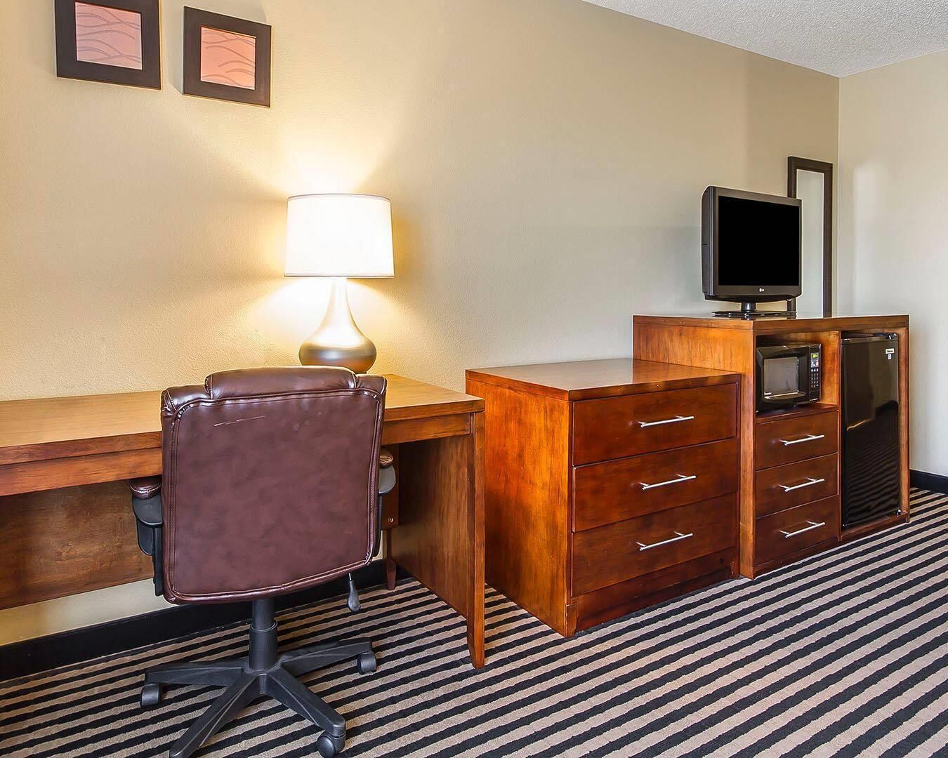 Una habitación de hotel con un escritorio de madera, un sillón de cuero, una lámpara, un televisor y un minibar.