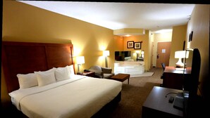 A hotel room with a large bed, a desk, a chair, a desk lamp, a nightstand, a mirror, a bathroom with a sink and a bathtub, and a door leading to another room. - Comfort Inn Owatonna near Medical Center (Owatonna)