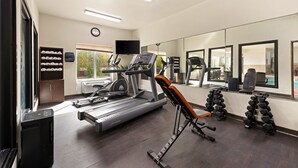 Un gimnasio con cinta de correr, banco de pesas y mancuernas.