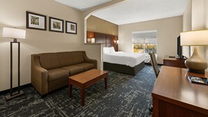 Habitación de hotel con sofá, cama, escritorio y lámpara. Se observan cuadros en la pared y una ventana con vistas.