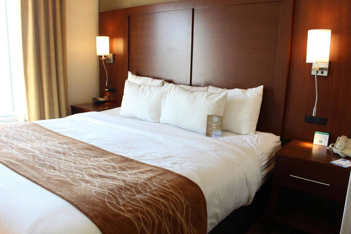 A hotel room with a large bed, two bedside tables, a nightstand, a lamp, and a sign indicating a 'Miss Our Planet' initiative.