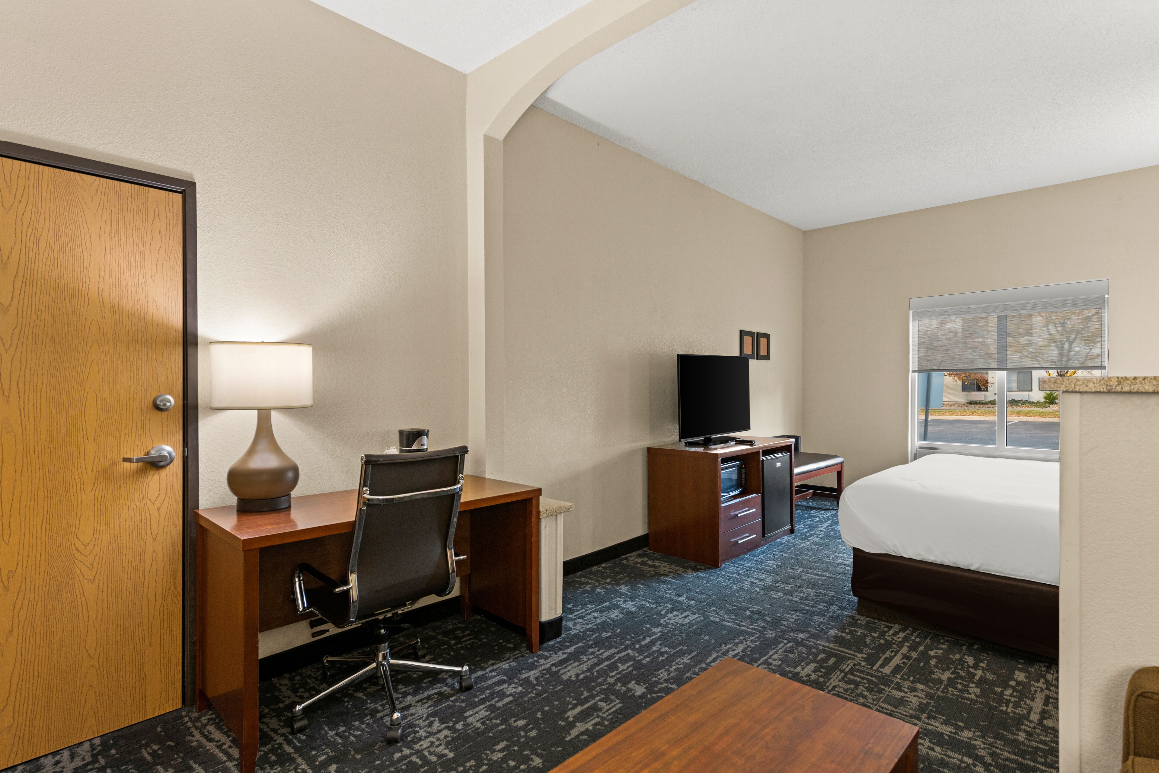 A hotel room with a desk, chair, television, bed, and a window with a view of the outside.