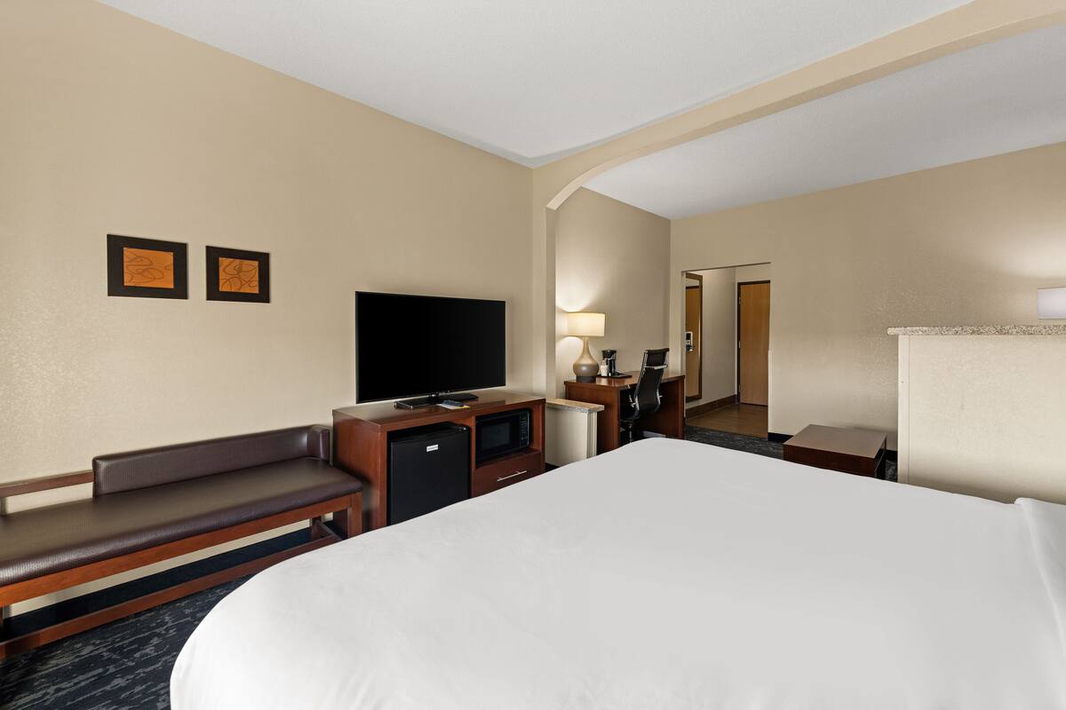 Une chambre d’hôtel avec un grand lit, une télévision, un bureau avec une lampe et un banc.