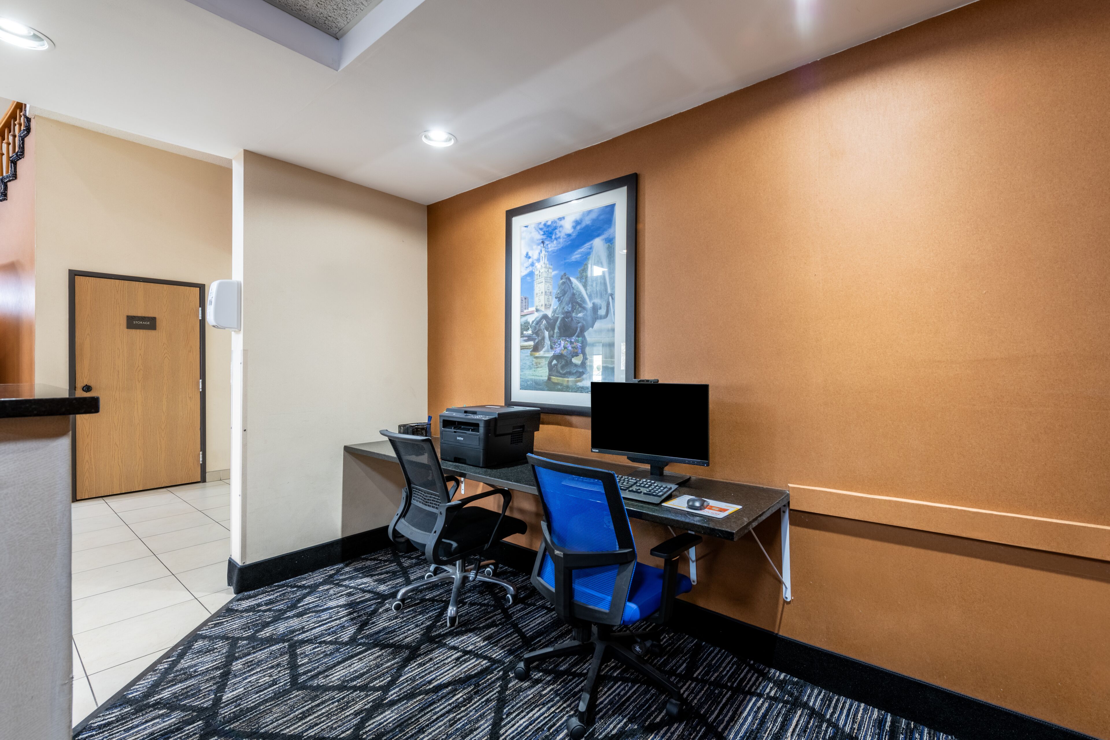 Una habitación de hotel con escritorio, dos sillas, computadora e impresora.