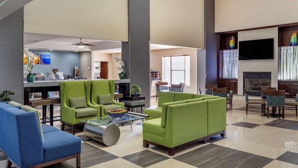A spacious lobby with green and blue seating, a coffee station, a fireplace, and a flat-screen TV on the wall.