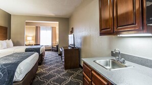 A hotel room with two beds, a kitchenette with a sink, and a television on a small table.