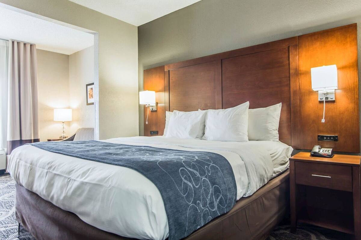 A hotel room with a large bed, bedside lamps, a phone on the nightstand, and a door leading to another room.