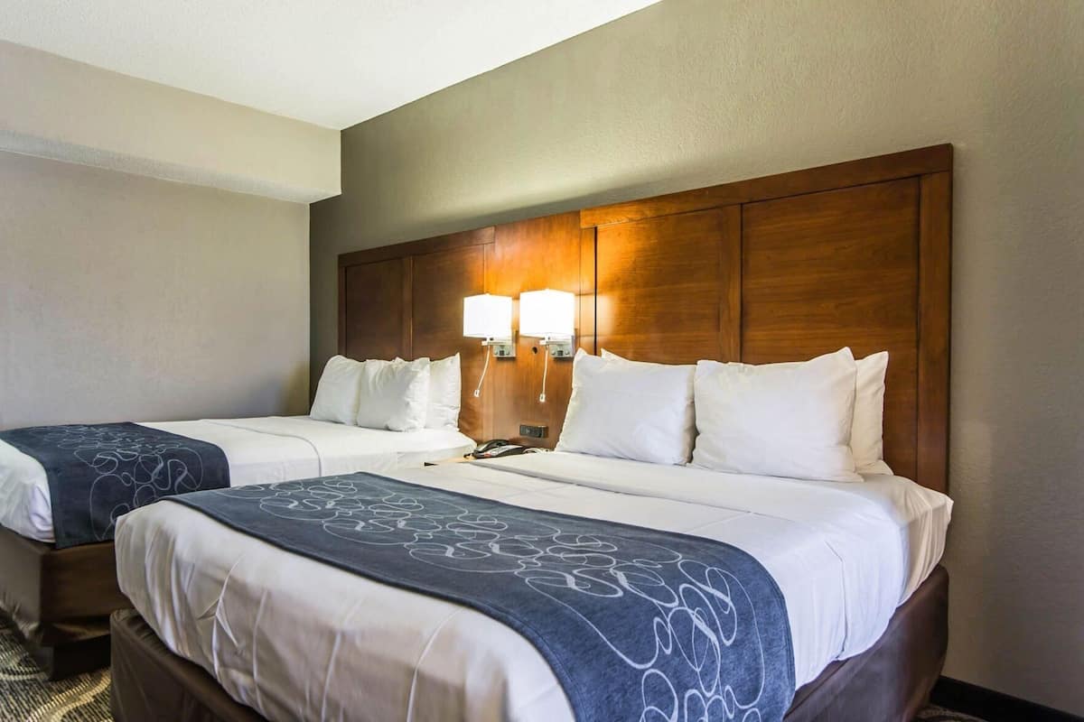 A hotel room with two beds, a wooden headboard, bedside lamps, and a telephone.