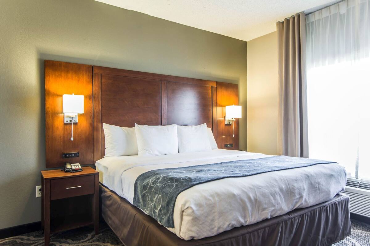 A hotel room with a large bed, two bedside lamps, a nightstand, and a window with curtains.