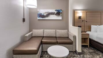 A modern hotel room with a sectional sofa, a small round table, a painting on the wall, and a wooden wardrobe.