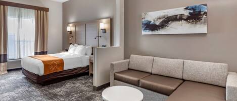 Una habitación de hotel con cama, sofá, mesa redonda y un cuadro en la pared.