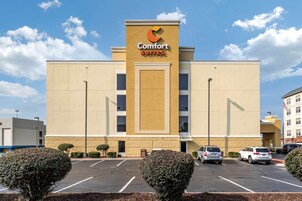 Un hotel Comfort Suites con fachada color beige, estacionamiento y dos arbustos bien cuidados al frente.