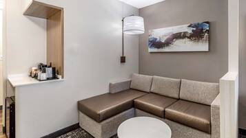 A modern hotel room with a sectional sofa, a small round table, a wall-mounted lamp, and a painting.