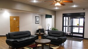 A living room with two black leather sofas, a round coffee table, and a wooden floor. There is a ceiling fan, a door, and a window with curtains. - Quality Inn Clinton - Knoxville North (Clinton)