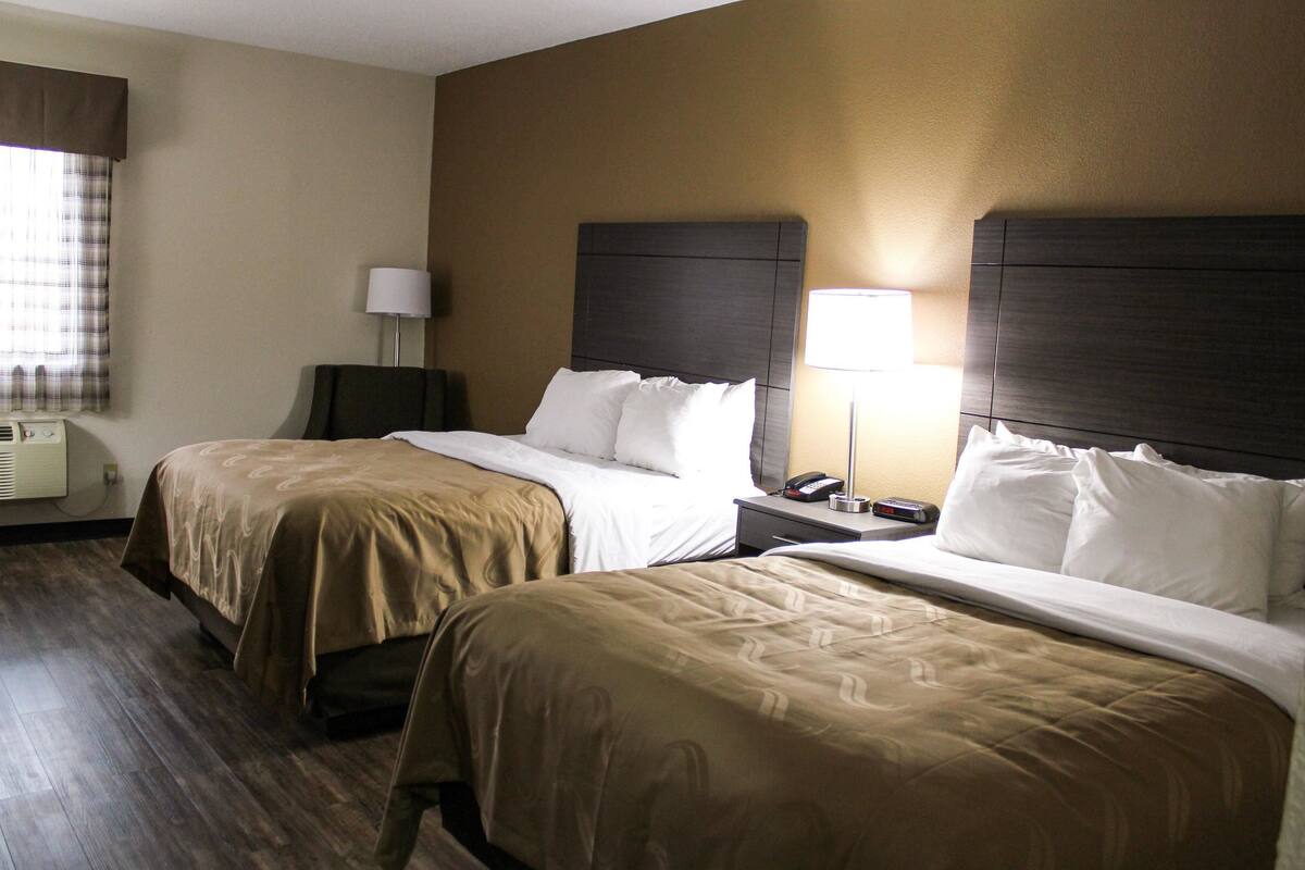 Une chambre d’hôtel avec deux lits, une table de chevet avec une lampe et un climatiseur fixé au mur.