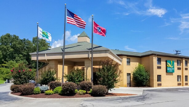A hotel with a covered entrance, American and state flags, and a Quality Inn sign. - Quality Inn Clinton - Knoxville North (Clinton)