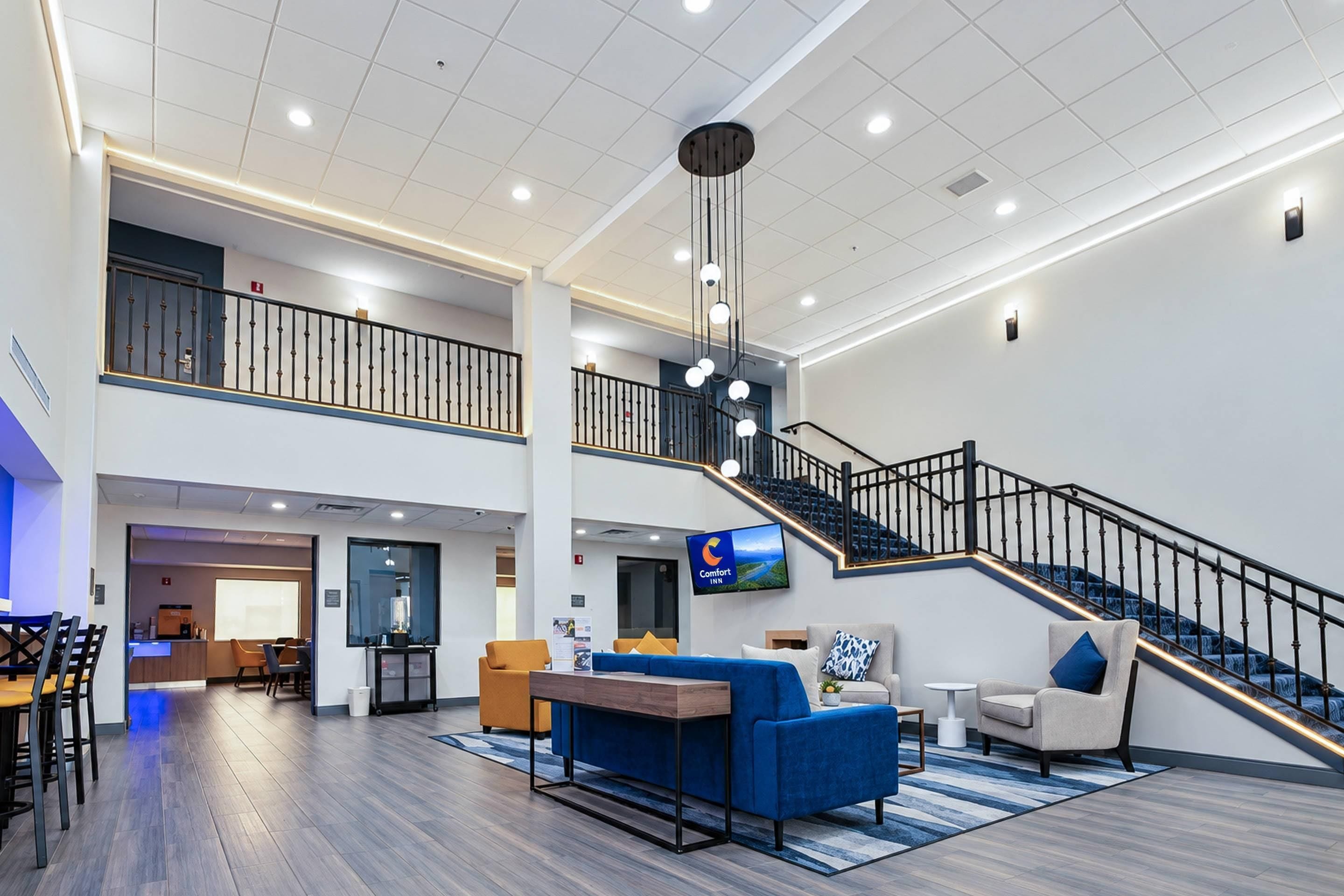 Eine geräumige Hotelhalle mit hoher Decke, einer Treppe und einer Sitzecke mit einem blauen Sofa und einem Couchtisch.