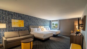 A hotel room with a bed, two bedside tables, a sofa, a chair, a small table, and a wall with a textured pattern.