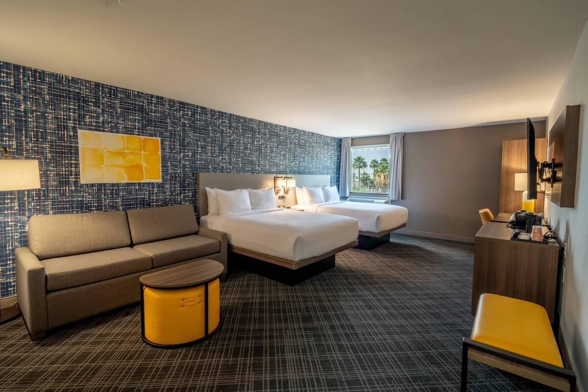 A hotel room with a bed, two bedside tables, a sofa, a chair, a small table, and a wall with a textured pattern.