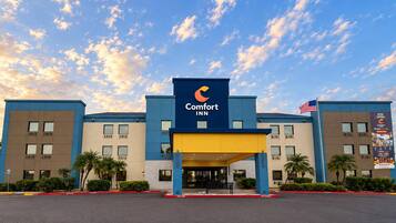 Un hotel Comfort Inn con fachada azul y amarilla, una bandera estadounidense y un cielo despejado con nubes.