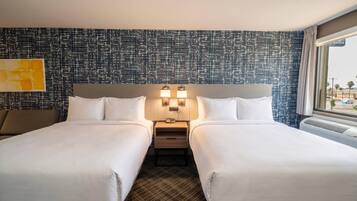 A hotel room with two beds, a nightstand with a lamp, a large window, and a patterned wall.