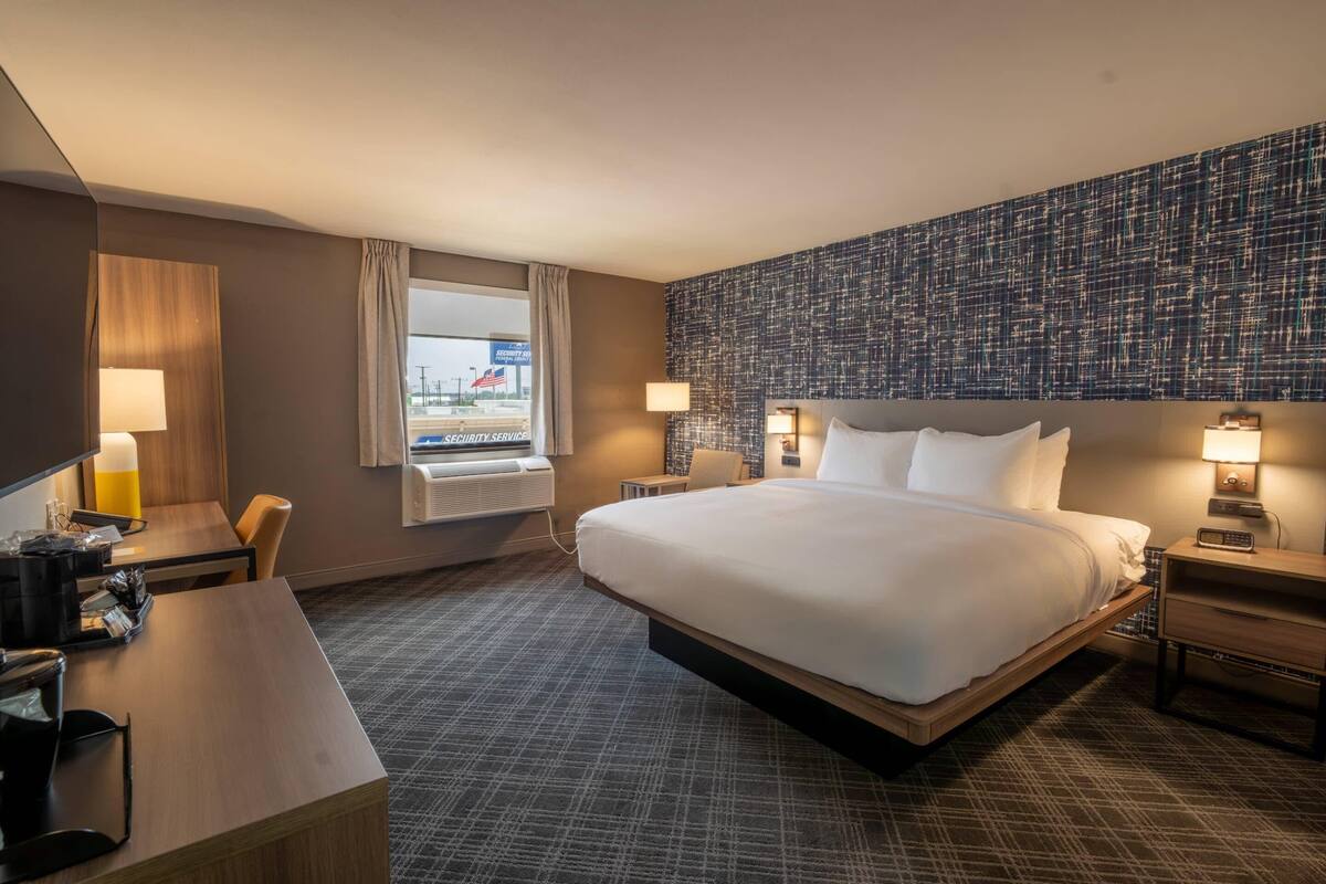 A hotel room with a large bed, a desk, a chair, a window with curtains, and a wall with a textured pattern.