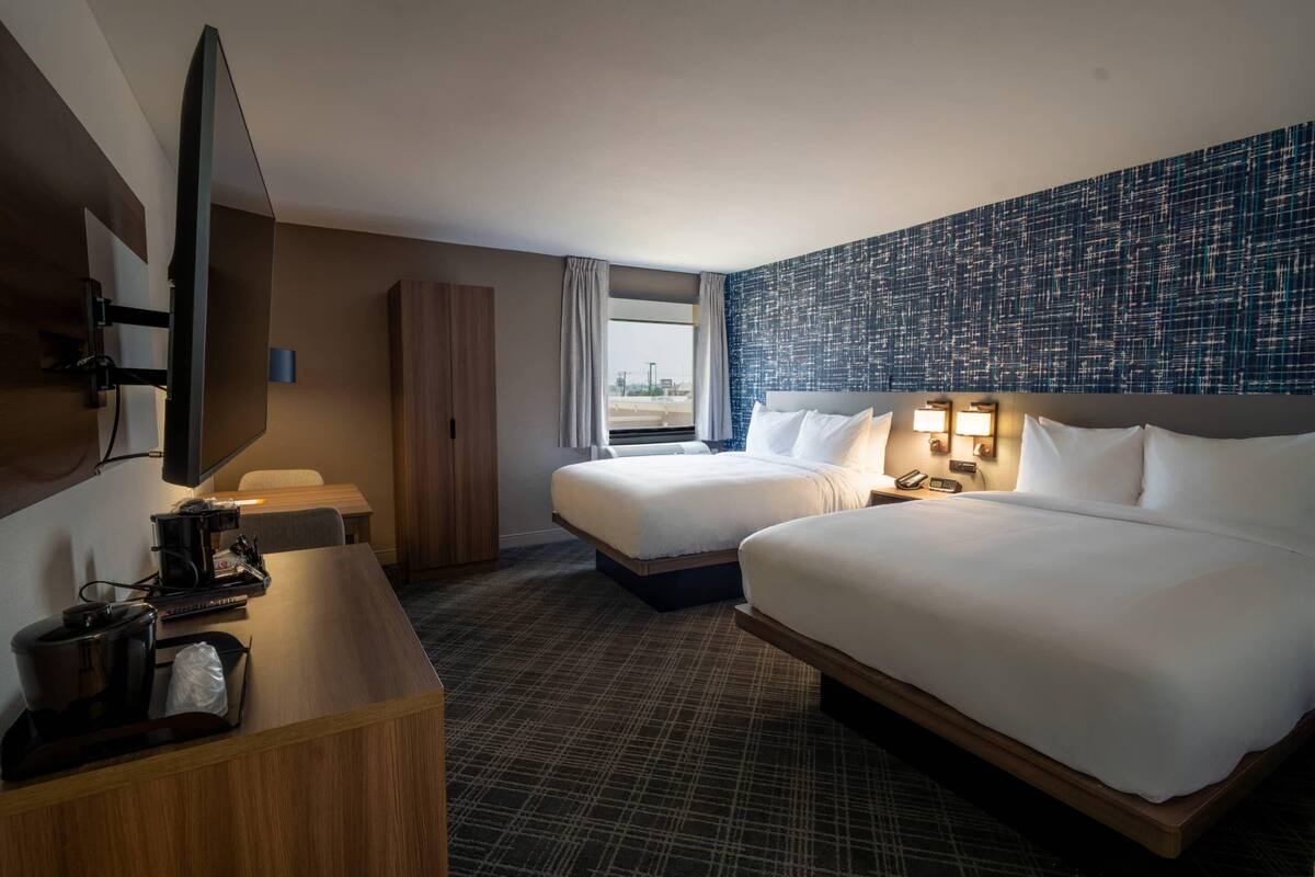 A hotel room with two beds, a desk with a coffee maker, a TV, and a city view.