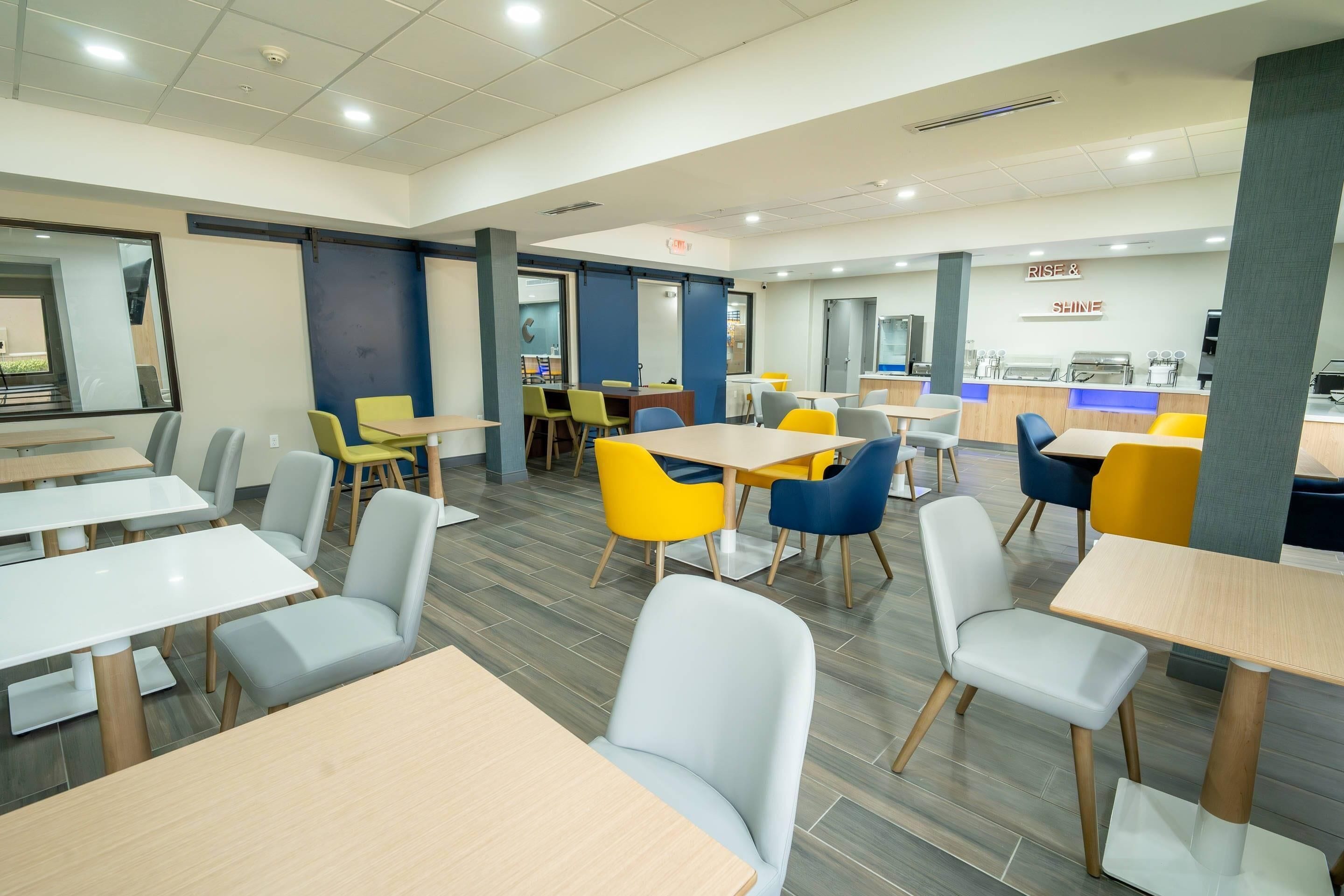 A modern dining area with multiple tables and chairs, a counter with a menu, and a visible exit sign.