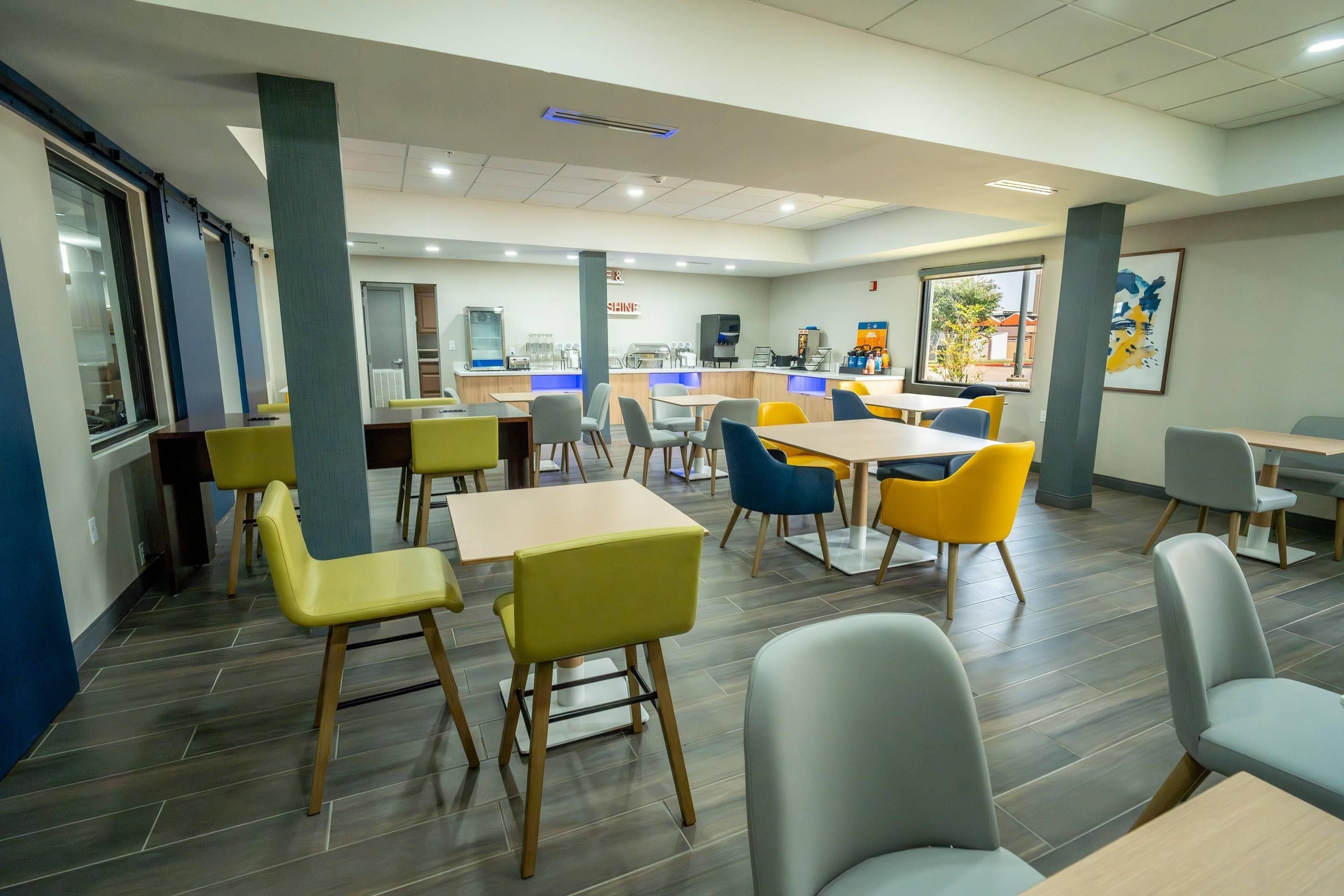 Un espace repas moderne avec des tables et des chaises, une machine à café et une grande fenêtre.
