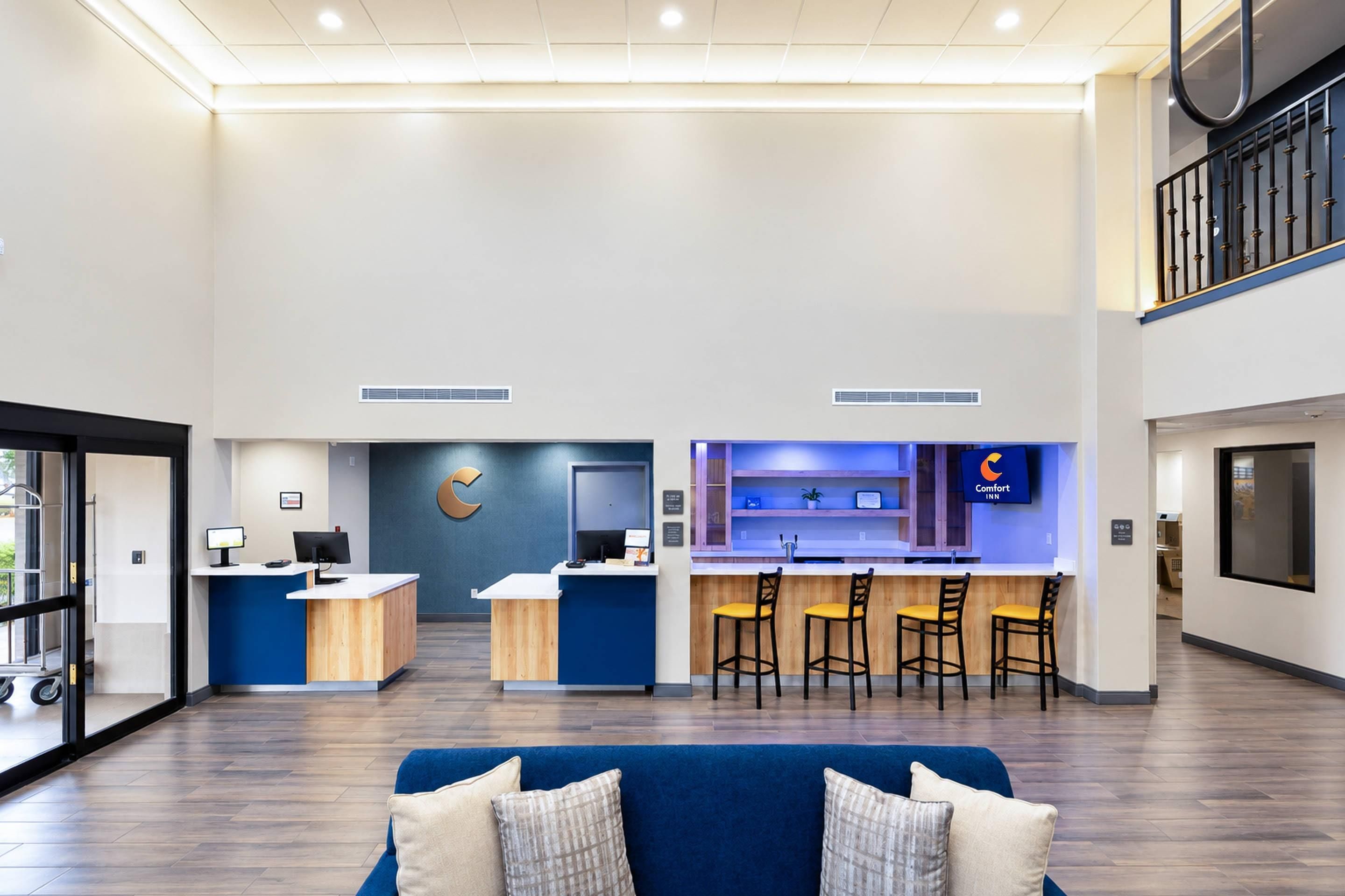 Un vestíbulo de hotel con mostrador de recepción, zona de bar y espacio de descanso con un sofá azul.