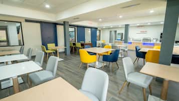 Un espace repas moderne avec plusieurs tables et chaises, un comptoir où est affiché le menu, et un panneau indiquant clairement la sortie.