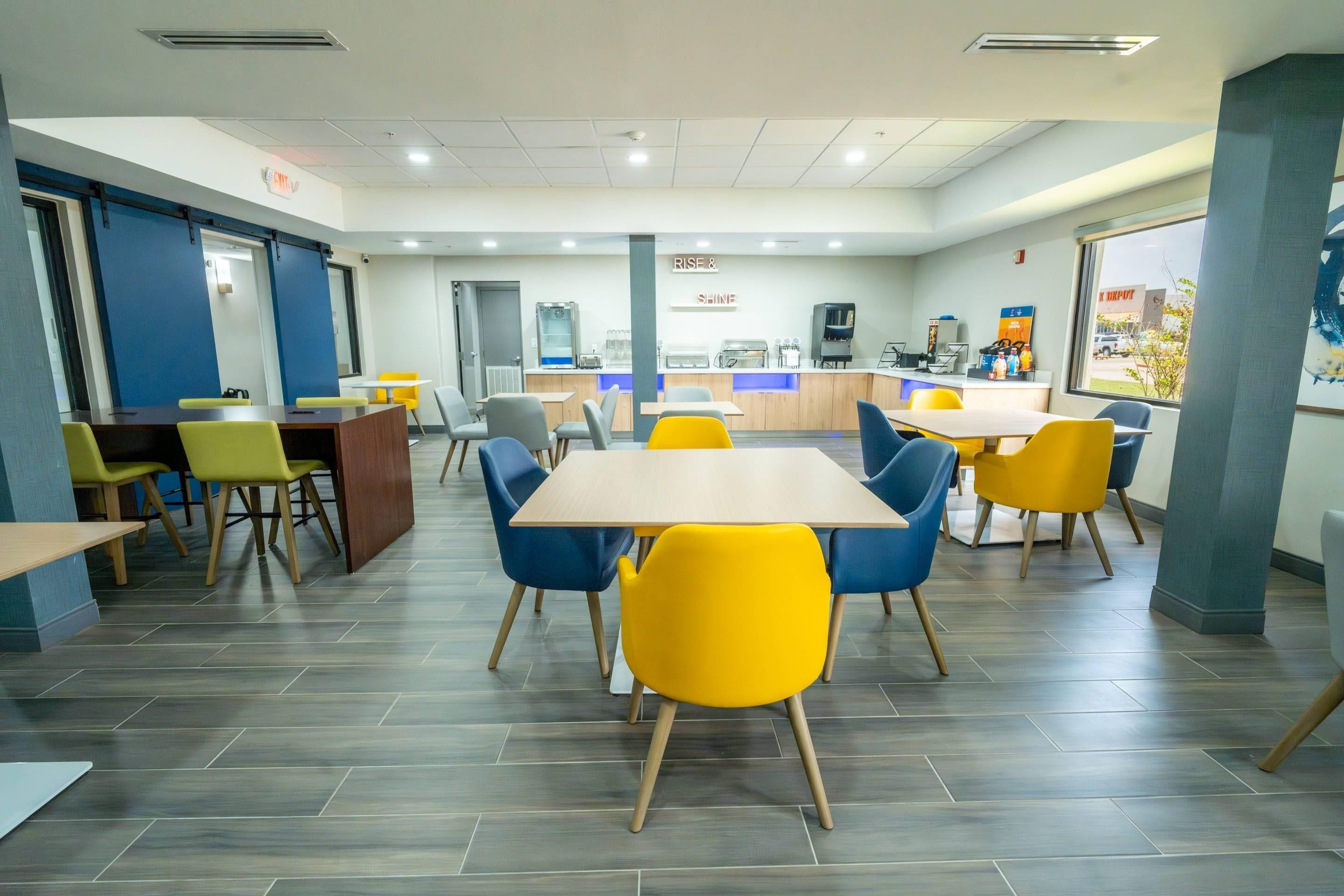 A modern dining area with tables and chairs, a counter with a coffee machine, and a view of the outside.