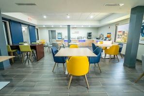 A modern dining area with tables and chairs, a counter with a coffee machine, and a view of the outside.