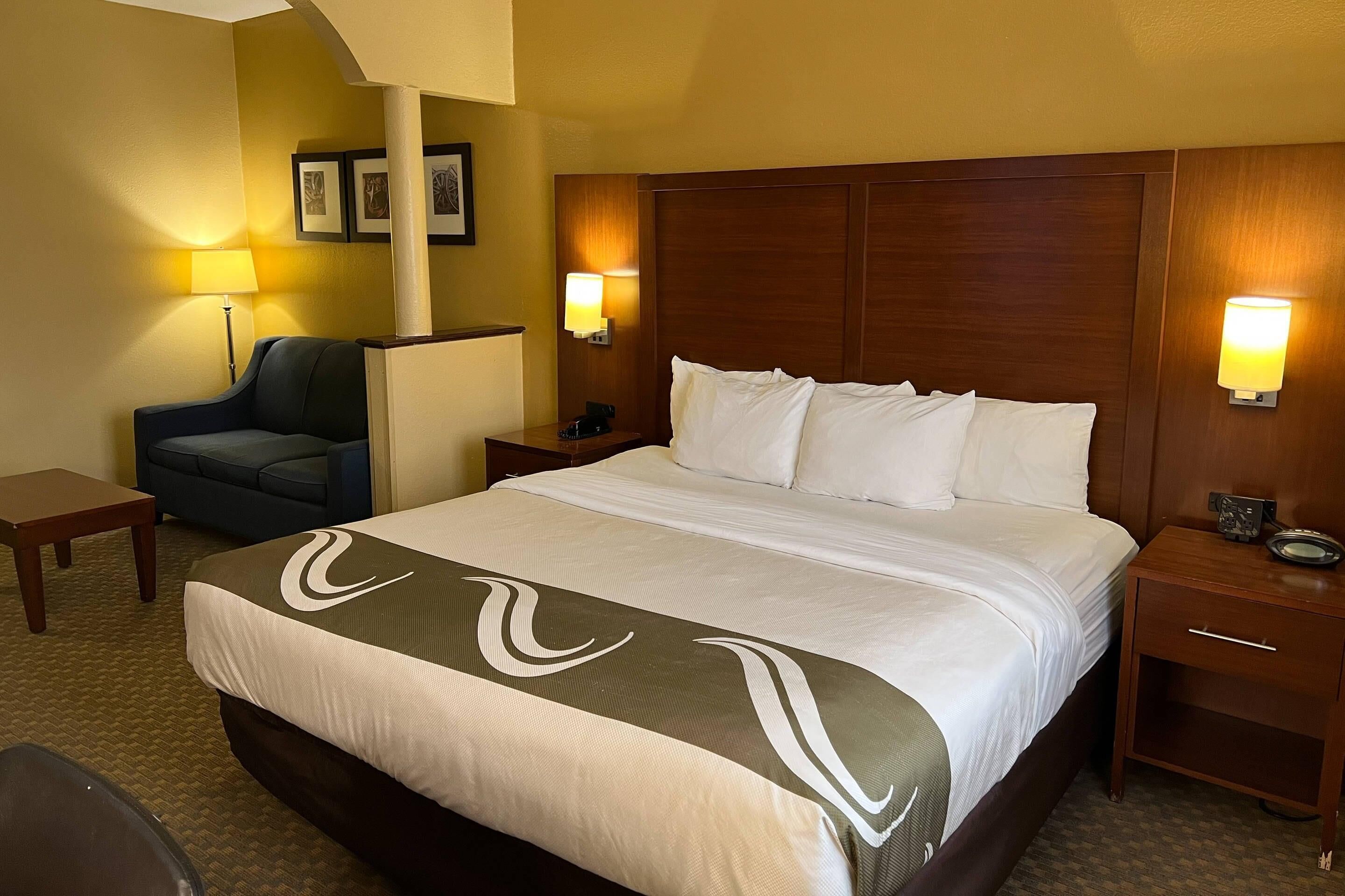 Una habitación de hotel con una cama grande, dos mesitas de noche, una silla y lámparas fijadas a la pared.