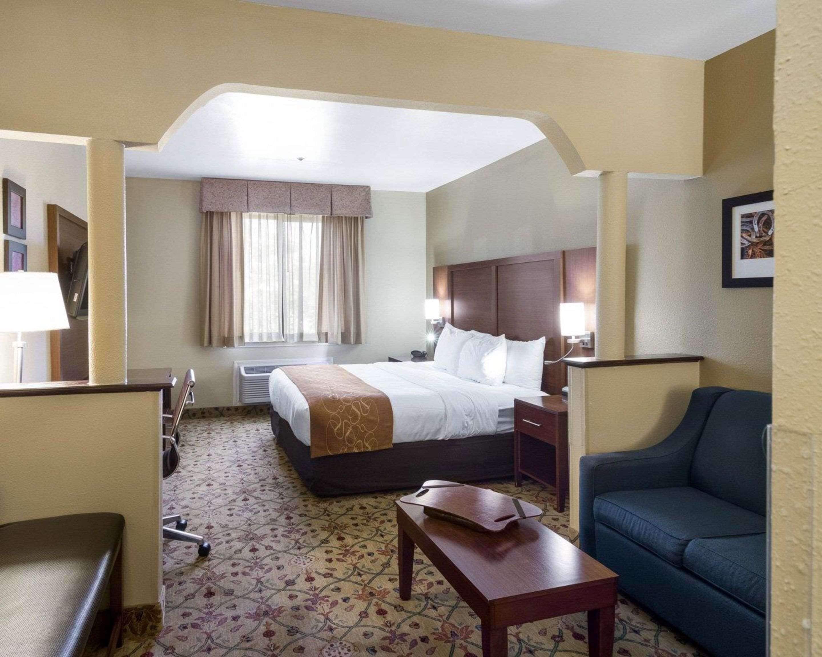 A hotel room with a bed, bedside table, chair, and a desk with a lamp.