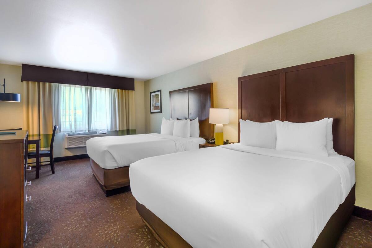 A hotel room with two beds, a desk, a chair, and a window with curtains.