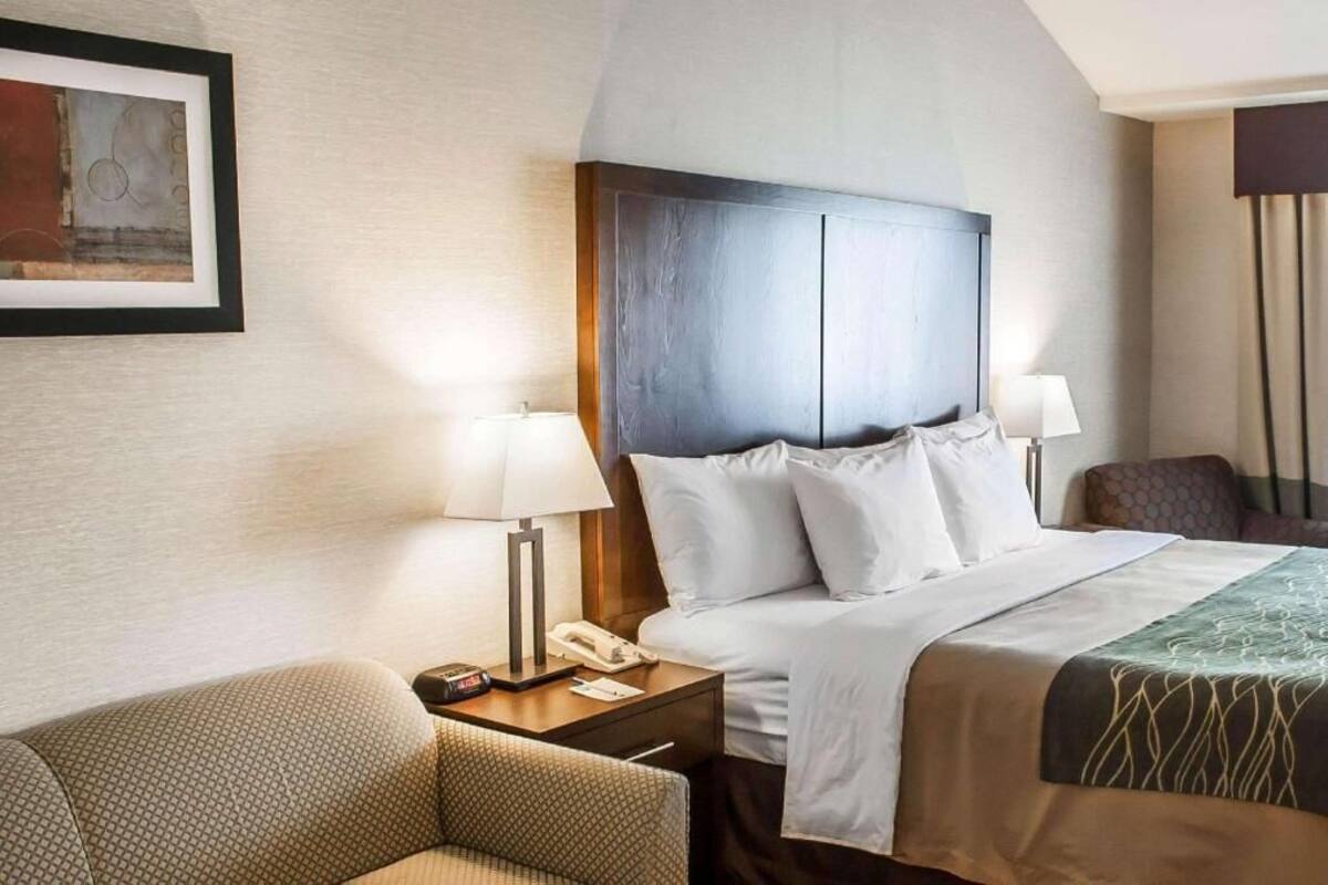 A hotel room with a bed, bedside lamps, a telephone, a chair, and a framed picture on the wall.