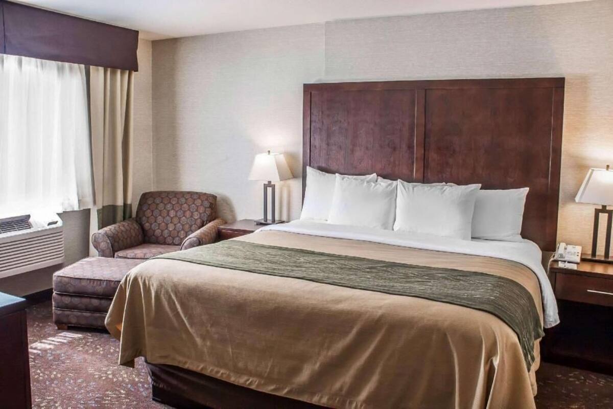 A hotel room with a large bed, a chair, a desk, and a lamp.