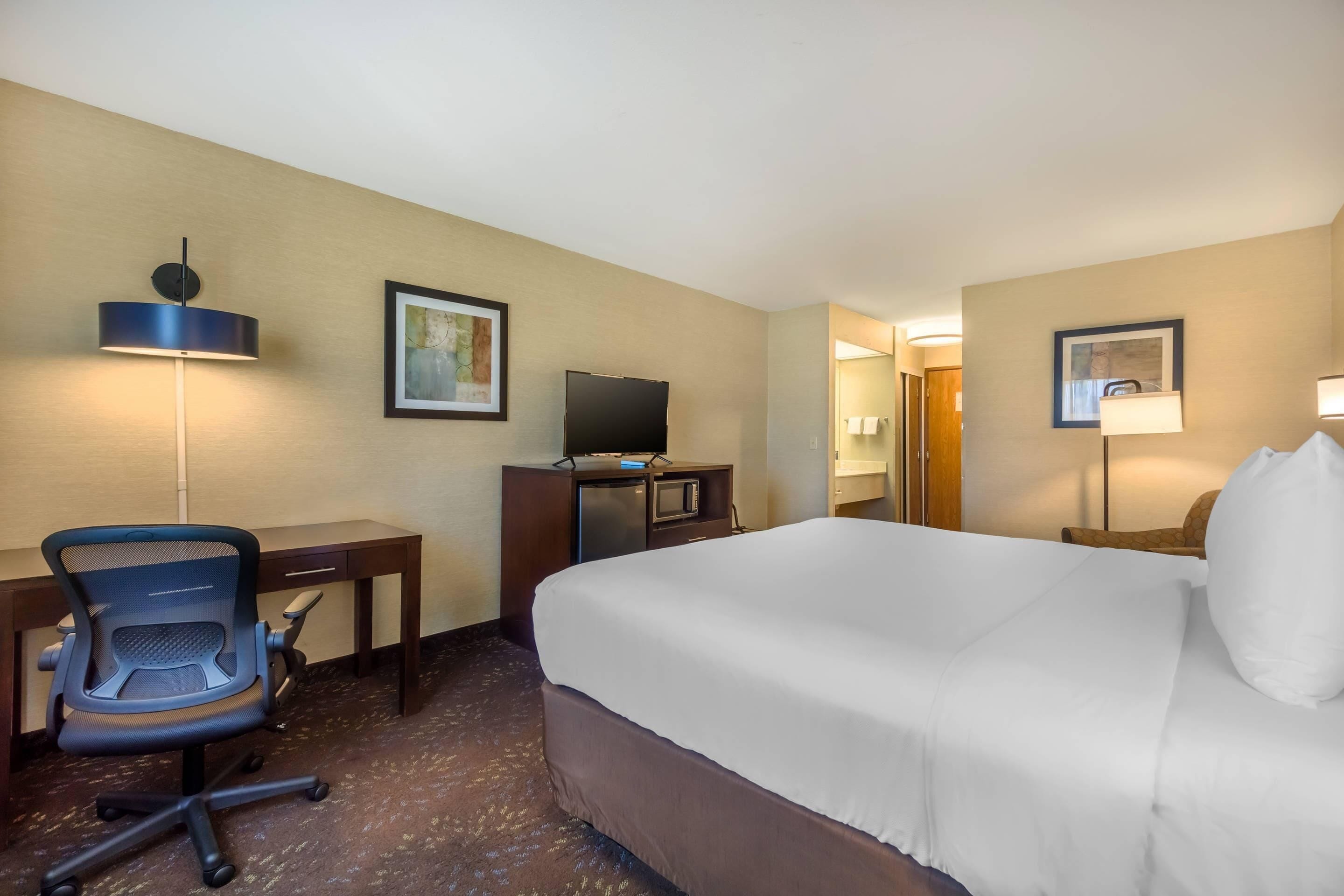 A hotel room with a bed, desk, chair, television, and lamps.