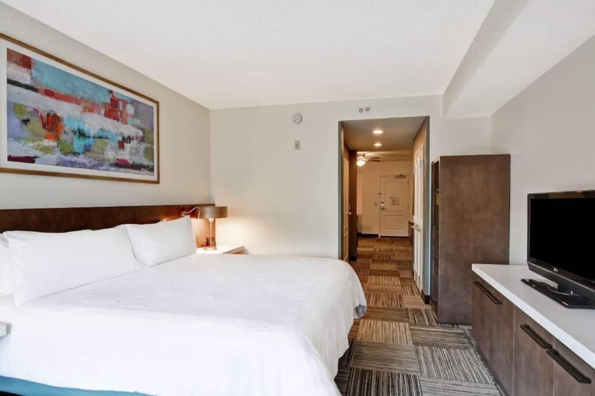 A hotel room with a bed, a TV, a painting, and a door leading to a bathroom.