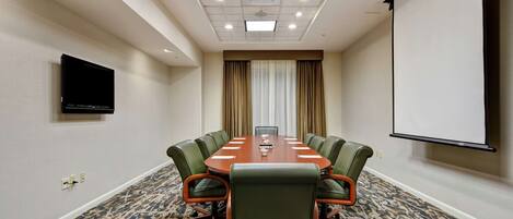 A conference room with a long table, six chairs, a projector screen, and a television on the wall.