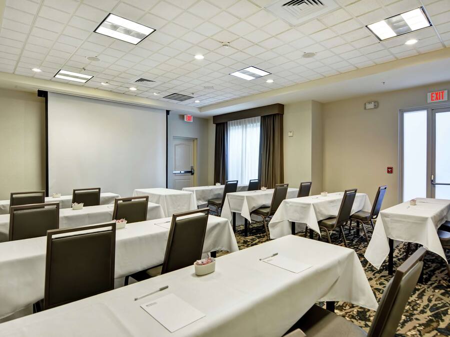 A conference room with multiple tables and chairs, a projector screen, and an exit sign.