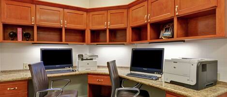 A corner office with two desks, two chairs, a clock, and wooden cabinets.