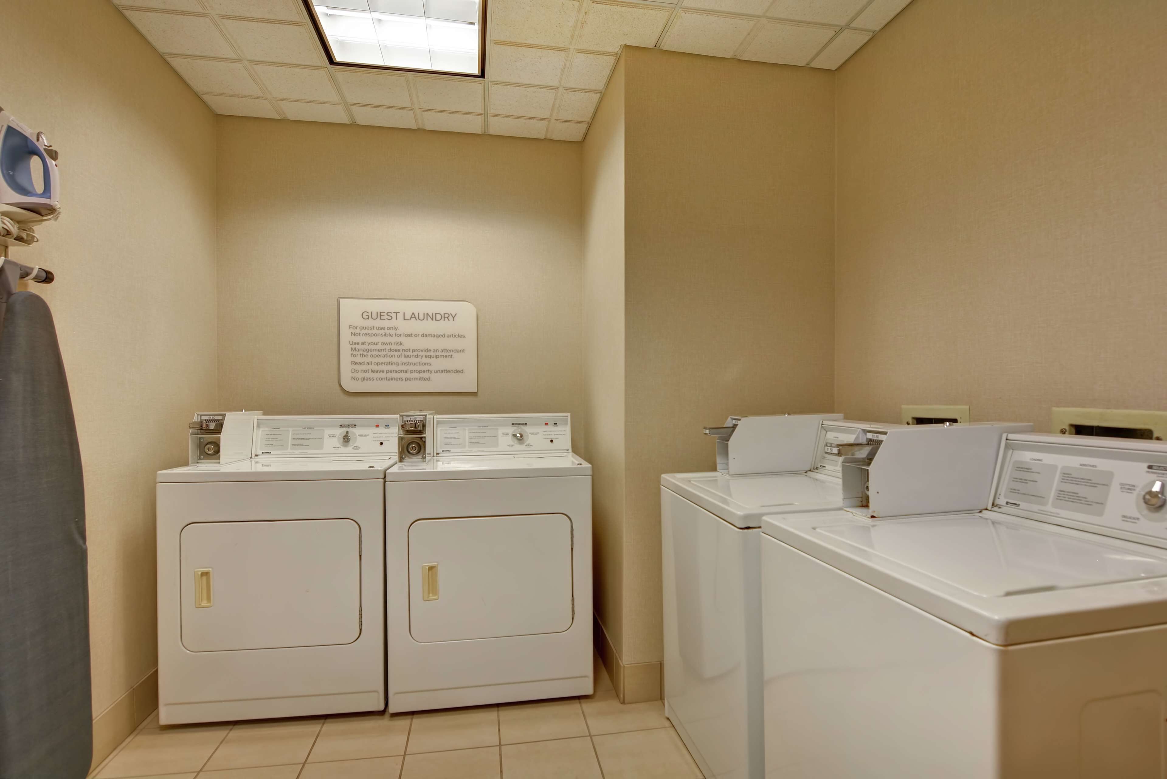 A laundry room with two front-loading washers and dryers, a sign indicating guest laundry rules, and a ceiling light.