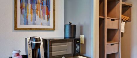 A kitchenette with a coffee maker, microwave, and a framed abstract painting on the wall.