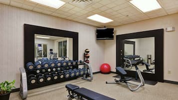 A gym with a bench, dumbbells, a red exercise ball, and a TV mounted on the wall.
